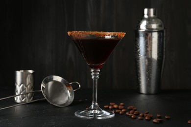 Photo of Martini cocktail with sugar in glass, coffee beans and shaker on black table, closeup