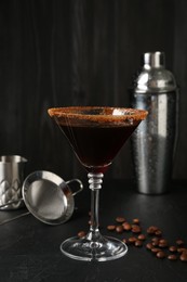 Photo of Martini cocktail with sugar in glass, coffee beans and shaker on black table, closeup