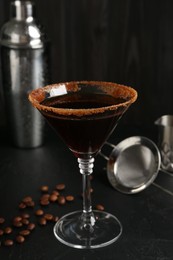 Photo of Martini cocktail with sugar in glass, coffee beans and shaker on black table, closeup