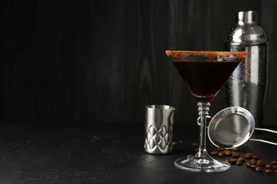 Photo of Martini cocktail with sugar in glass, coffee beans and shaker on black table, closeup. Space for text