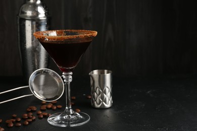 Photo of Martini cocktail with sugar in glass, coffee beans and shaker on black table, closeup. Space for text