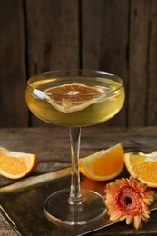 Photo of Martini cocktail in glass, orange slices and flower on wooden table, closeup