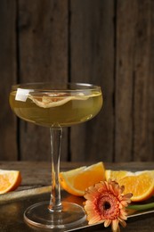 Photo of Martini cocktail in glass, orange slices and flower on wooden table, closeup