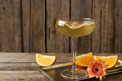 Photo of Martini cocktail in glass, orange slices and flower on wooden table, closeup. Space for text