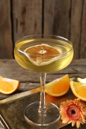 Photo of Martini cocktail in glass, orange slices and flower on wooden table, closeup