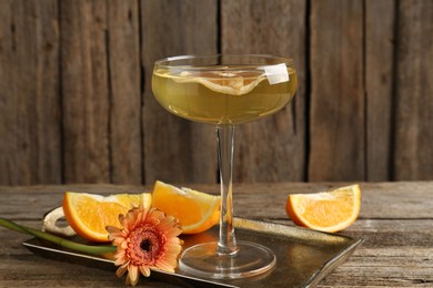 Photo of Martini cocktail in glass, orange slices and flower on wooden table, closeup