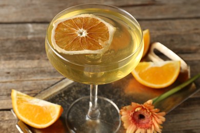 Photo of Martini cocktail in glass, orange slices and flower on wooden table, closeup