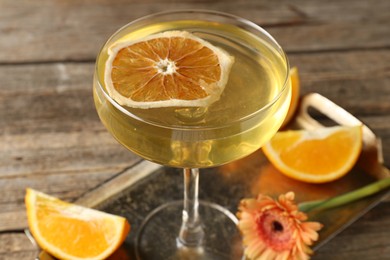 Photo of Martini cocktail in glass, orange slices and flower on wooden table, closeup