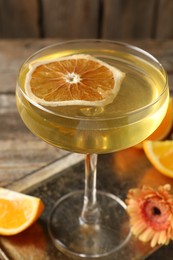 Photo of Martini cocktail in glass, orange slices and flower on wooden table, closeup