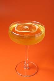 Photo of Martini cocktail with orange slice in glass on orange background, closeup