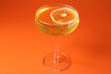 Photo of Martini cocktail with orange slice in glass on orange background, closeup