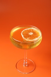 Photo of Martini cocktail with orange slice in glass on orange background, closeup