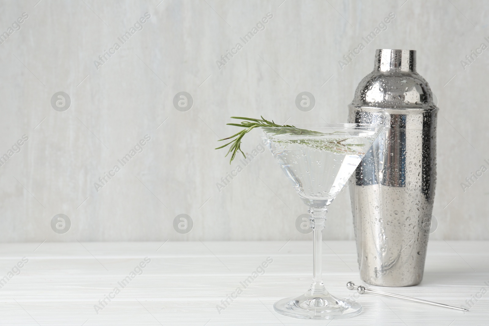 Martini cocktail with rosemary in glass and shaker on white wooden table, closeup. Space for text Photo of Martini cocktail with rosemary in glass and shaker on white wooden table, closeup. Space for text