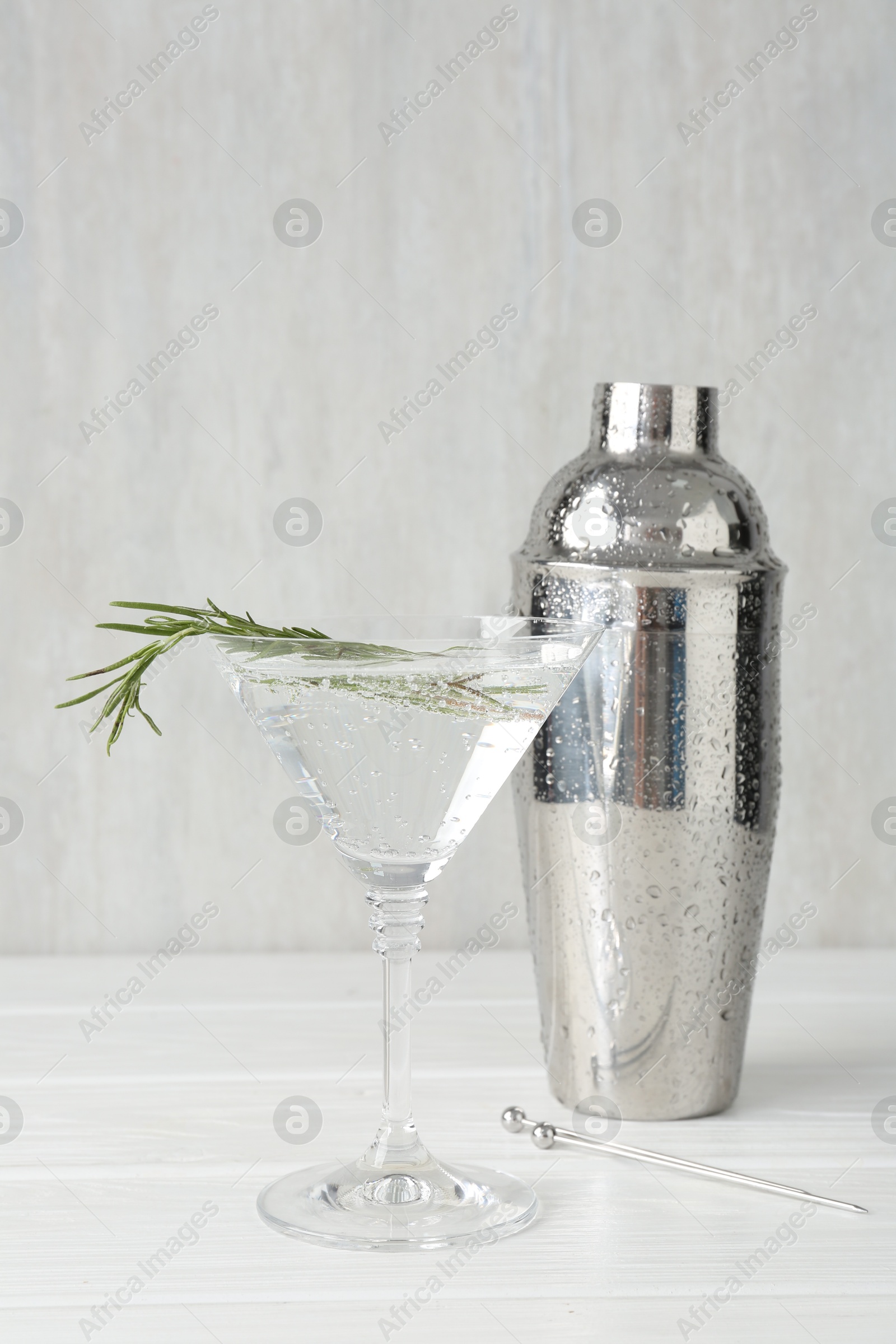 Martini cocktail with rosemary in glass and shaker on white wooden table, closeup Photo of Martini cocktail with rosemary in glass and shaker on white wooden table, closeup