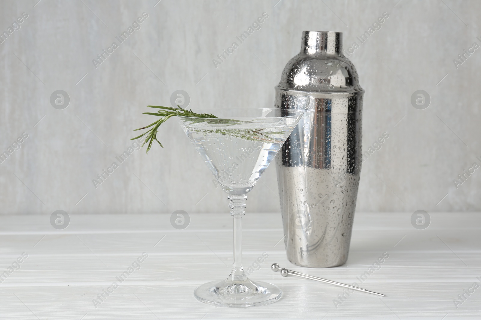 Martini cocktail with rosemary in glass and shaker on white wooden table, closeup Photo of Martini cocktail with rosemary in glass and shaker on white wooden table, closeup