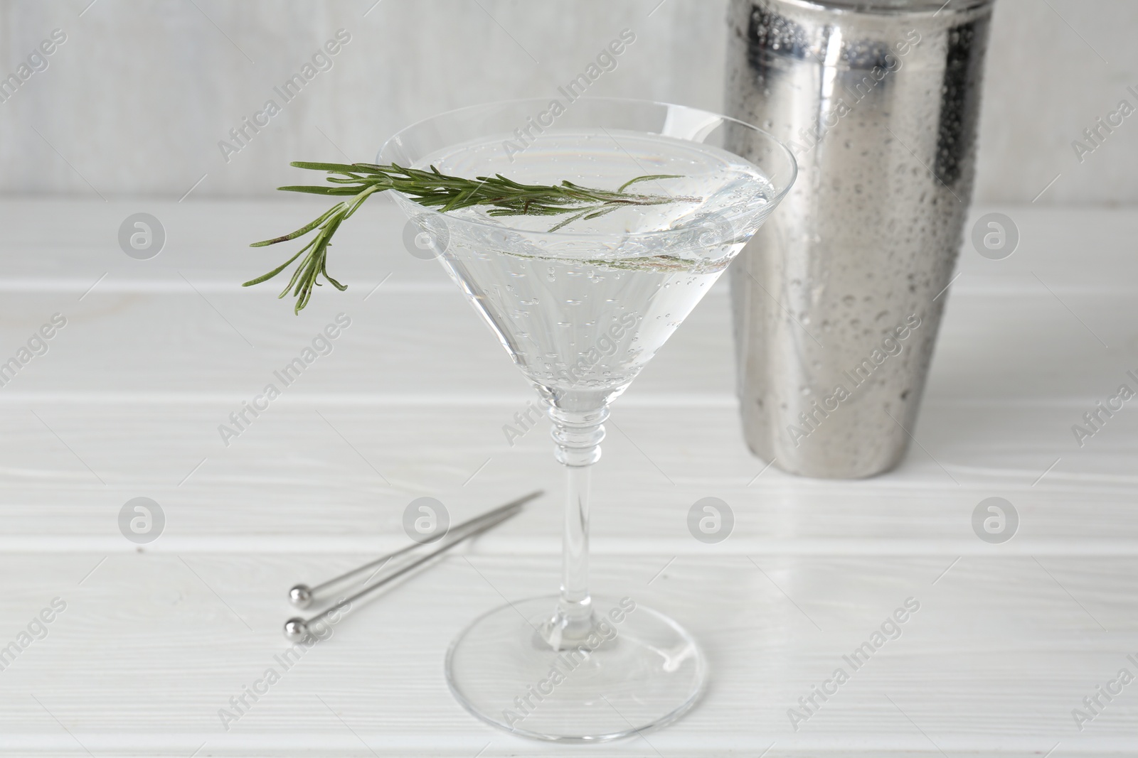 Martini cocktail with rosemary in glass and shaker on white wooden table, closeup Photo of Martini cocktail with rosemary in glass and shaker on white wooden table, closeup