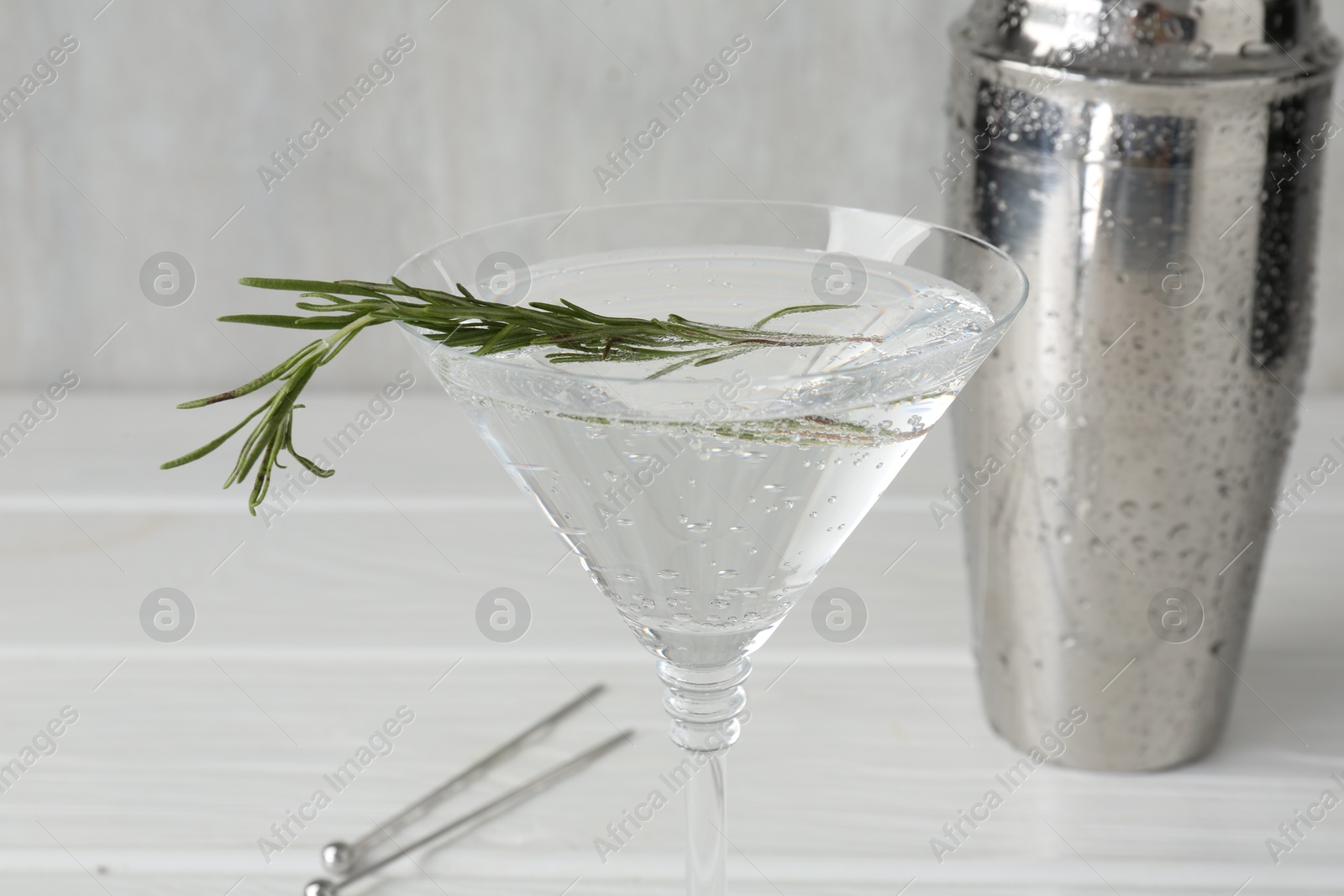 Martini cocktail with rosemary in glass and shaker on white wooden table, closeup Photo of Martini cocktail with rosemary in glass and shaker on white wooden table, closeup
