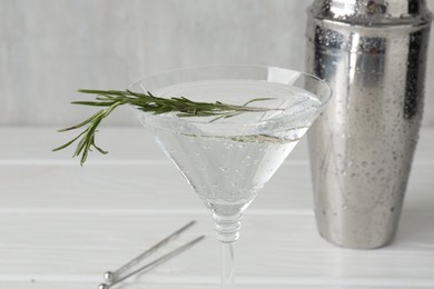 Photo of Martini cocktail with rosemary in glass and shaker on white wooden table, closeup