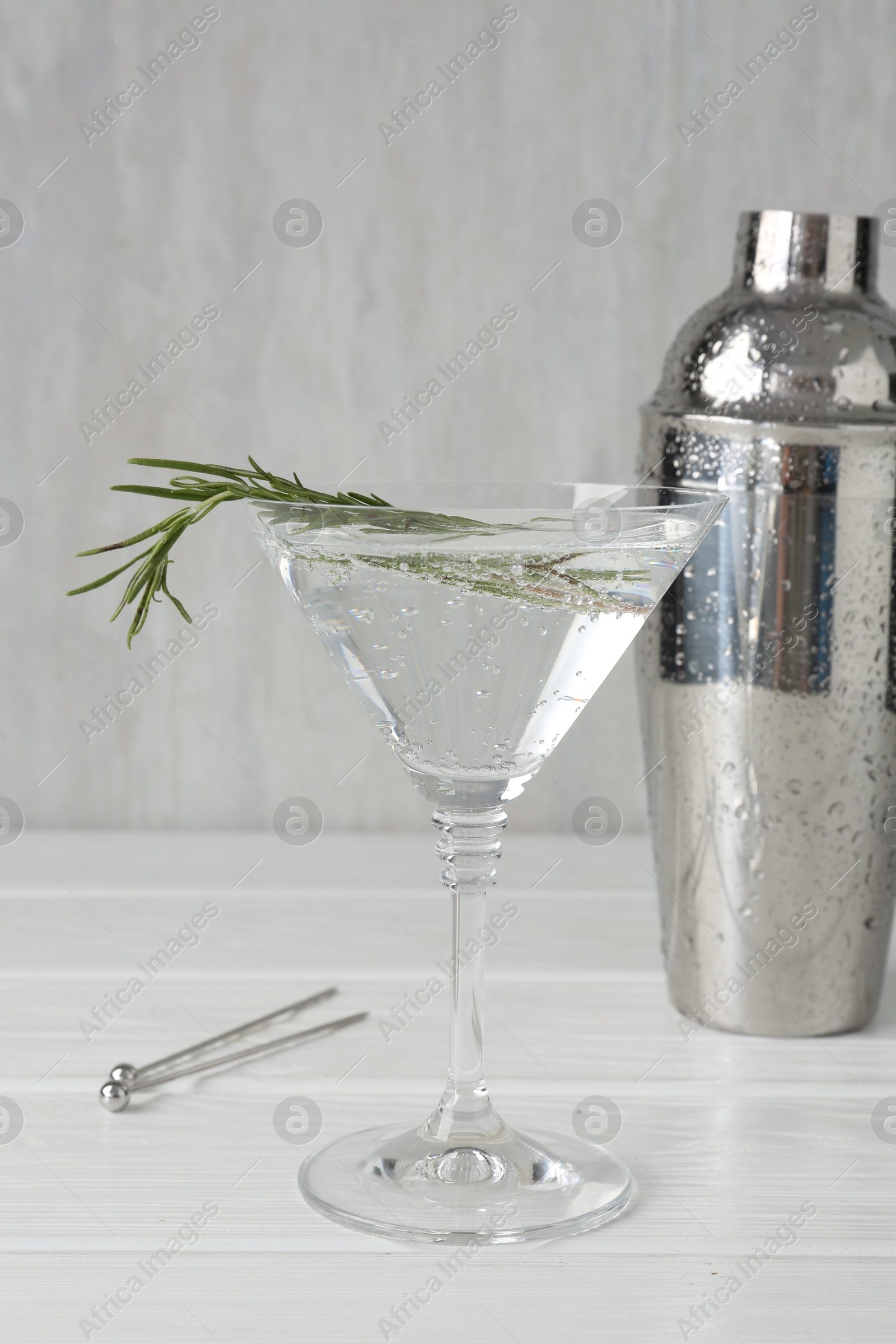Martini cocktail with rosemary in glass and shaker on white wooden table, closeup Photo of Martini cocktail with rosemary in glass and shaker on white wooden table, closeup