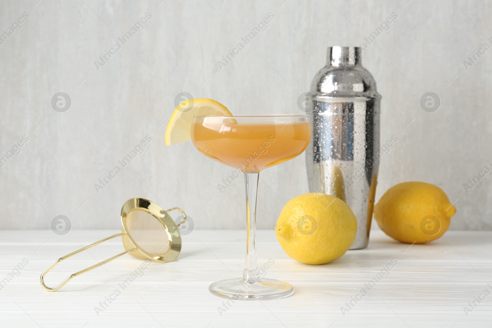Martini cocktail with lemon slice in glass, fruits and shaker on white wooden table, closeup Photo of Martini cocktail with lemon slice in glass, fruits and shaker on white wooden table, closeup
