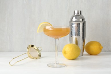 Photo of Martini cocktail with lemon slice in glass, fruits and shaker on white wooden table, closeup