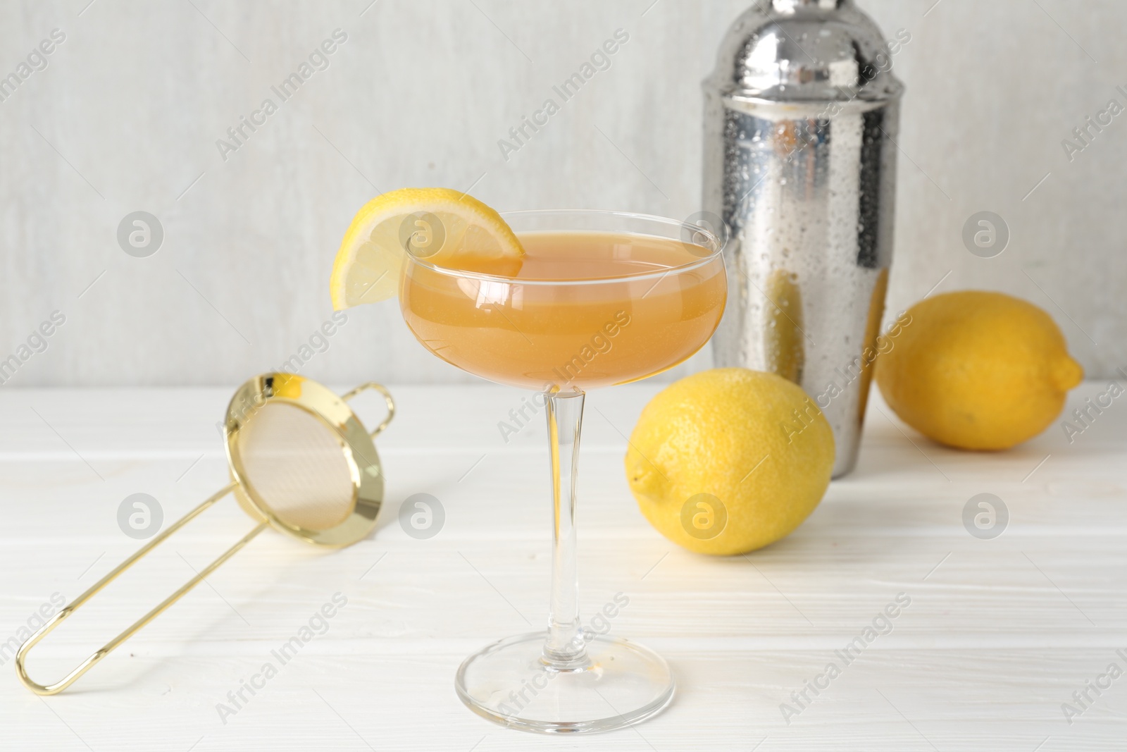Martini cocktail with lemon slice in glass, fruits and shaker on white wooden table, closeup Photo of Martini cocktail with lemon slice in glass, fruits and shaker on white wooden table, closeup
