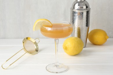 Photo of Martini cocktail with lemon slice in glass, fruits and shaker on white wooden table, closeup