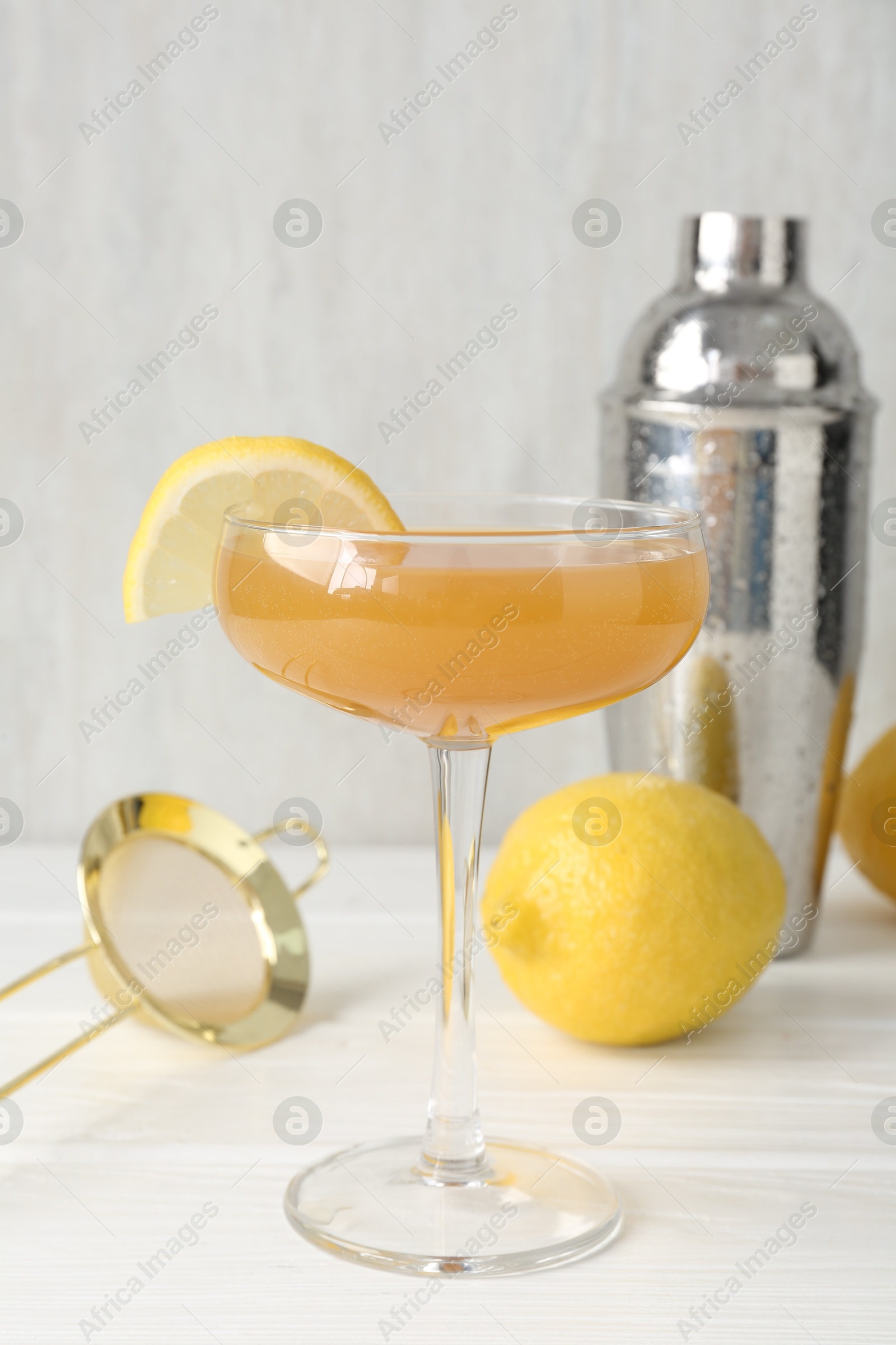 Martini cocktail with lemon slice in glass, fruit and shaker on white wooden table, closeup Photo of Martini cocktail with lemon slice in glass, fruit and shaker on white wooden table, closeup