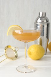 Photo of Martini cocktail with lemon slice in glass, fruit and shaker on white wooden table, closeup