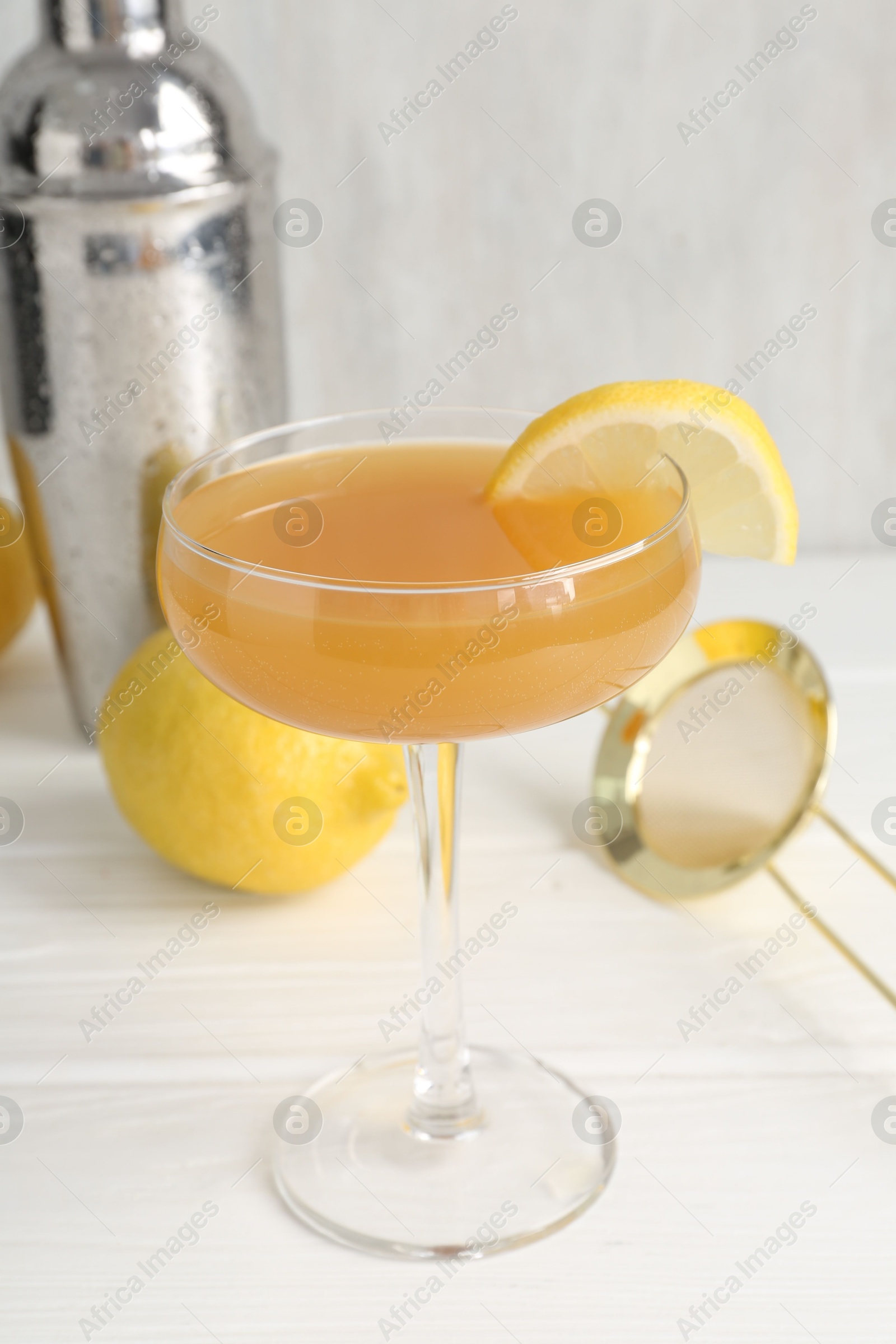 Martini cocktail with lemon slice in glass, fruit and shaker on white wooden table, closeup Photo of Martini cocktail with lemon slice in glass, fruit and shaker on white wooden table, closeup
