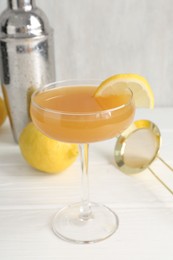 Photo of Martini cocktail with lemon slice in glass, fruit and shaker on white wooden table, closeup