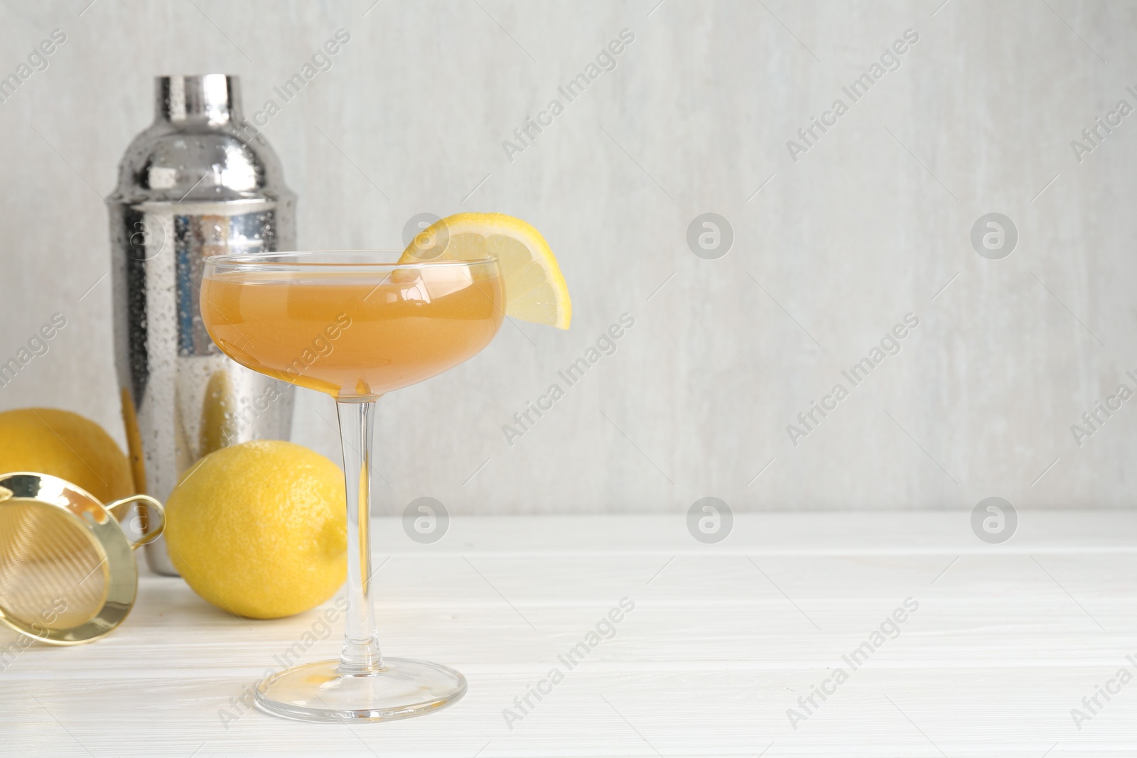 Martini cocktail with lemon slice in glass, fruits and shaker on white wooden table, closeup. Space for text Photo of Martini cocktail with lemon slice in glass, fruits and shaker on white wooden table, closeup. Space for text
