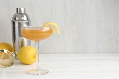 Photo of Martini cocktail with lemon slice in glass, fruits and shaker on white wooden table, closeup. Space for text