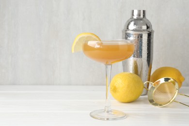 Photo of Martini cocktail with lemon slice in glass, fruits and shaker on white wooden table, closeup. Space for text