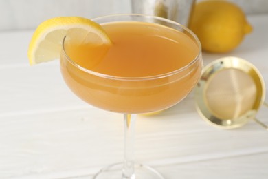 Photo of Martini cocktail with lemon slice in glass and fruit on white wooden table, closeup
