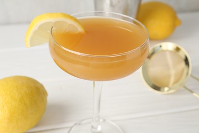 Photo of Martini cocktail with lemon slice in glass and fruits on white wooden table, closeup