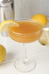 Photo of Martini cocktail with lemon slice in glass, fruits and shaker on white wooden table, closeup