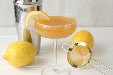 Photo of Martini cocktail with lemon slice in glass, fruits and shaker on white wooden table, closeup