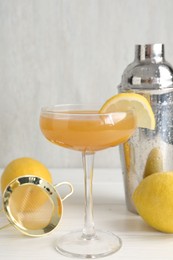 Photo of Martini cocktail with lemon slice in glass, fruits and shaker on white wooden table, closeup