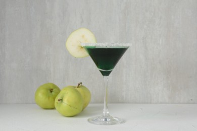 Photo of Martini cocktail with apple slice in glass and fruits on white table, closeup