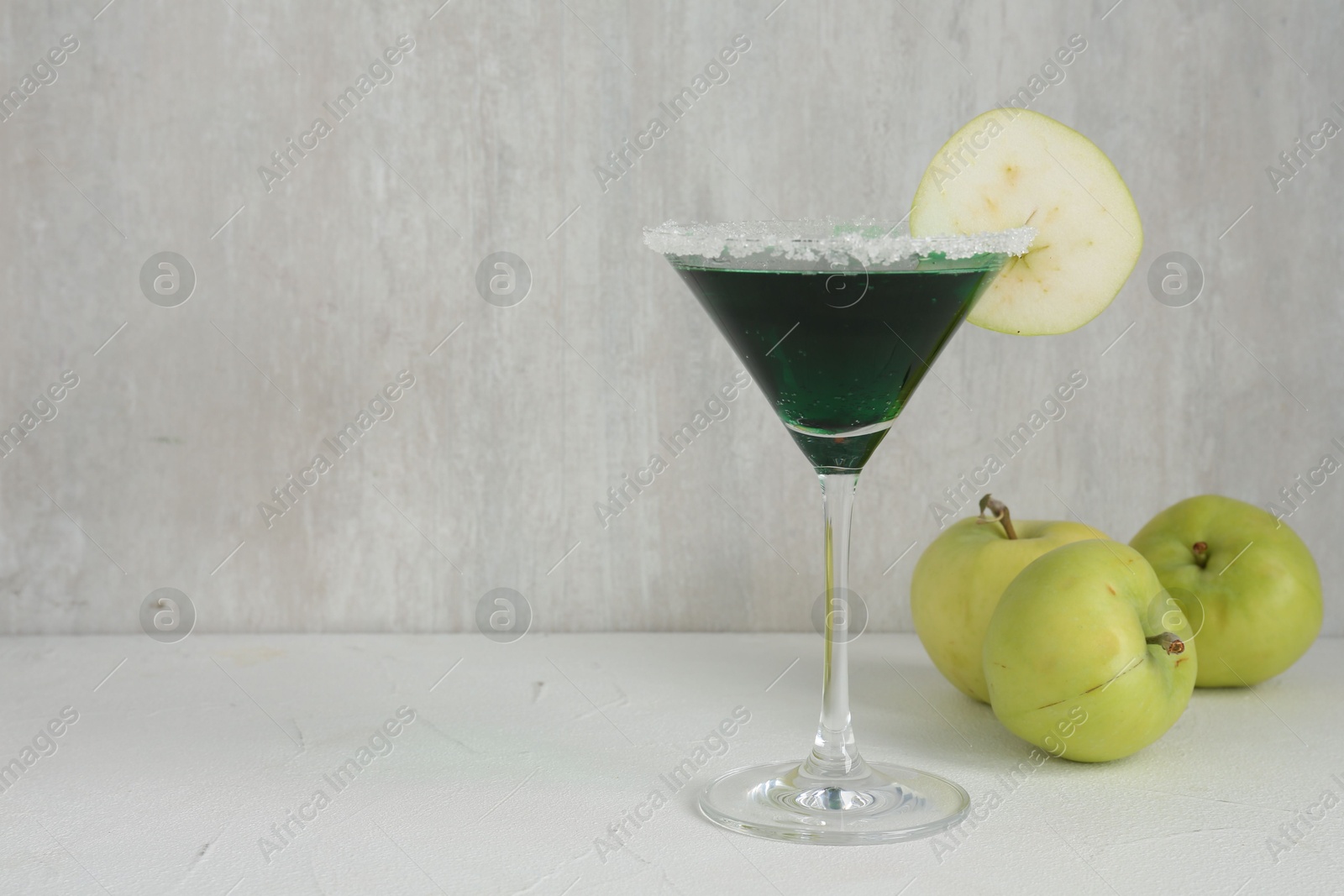 Martini cocktail with apple slice in glass and fruits on white table, closeup. Space for text Photo of Martini cocktail with apple slice in glass and fruits on white table, closeup. Space for text