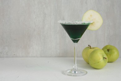 Photo of Martini cocktail with apple slice in glass and fruits on white table, closeup. Space for text
