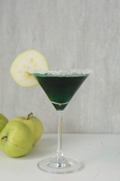Photo of Martini cocktail with apple slice in glass and fruits on white table, closeup
