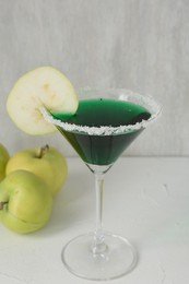 Photo of Martini cocktail with apple slice in glass and fruits on white table, closeup