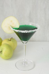 Photo of Martini cocktail with apple slice in glass and fruits on white table, closeup