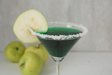 Photo of Martini cocktail with apple slice in glass and fruits on white table, closeup