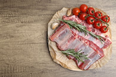 Photo of Fresh raw beef ribs, tomatoes and spices on wooden table, top view. Space for text