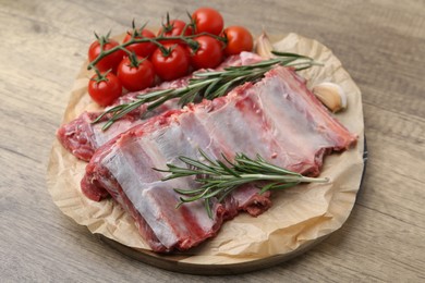 Photo of Fresh raw beef ribs, tomatoes and spices on wooden table, closeup