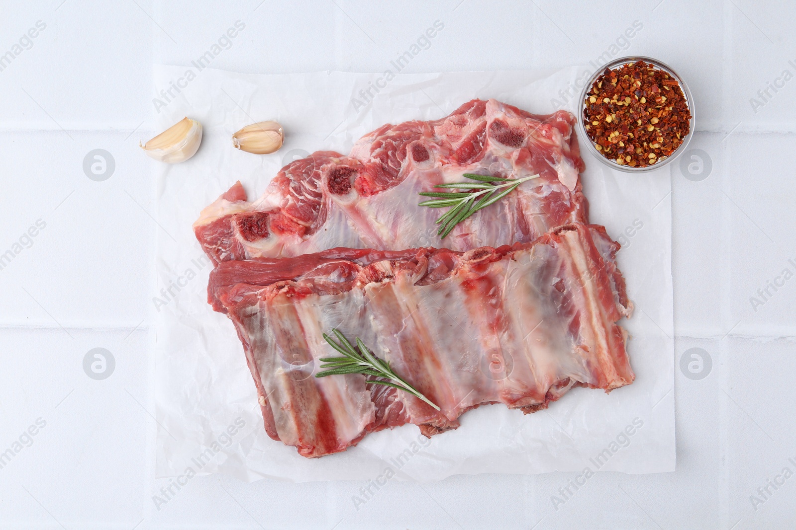 Photo of Fresh raw beef ribs and spices on white tiled table, flat lay