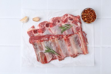 Photo of Fresh raw beef ribs and spices on white tiled table, flat lay